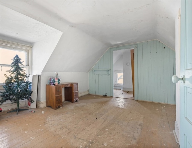 bonus room featuring a wealth of natural light, lofted ceiling, light hardwood / wood-style floors, and wood walls