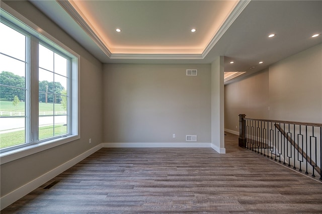 empty room featuring wood-type flooring, a tray ceiling, and crown molding