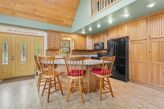 kitchen featuring backsplash, light stone counters, black appliances, a kitchen island, and a breakfast bar area