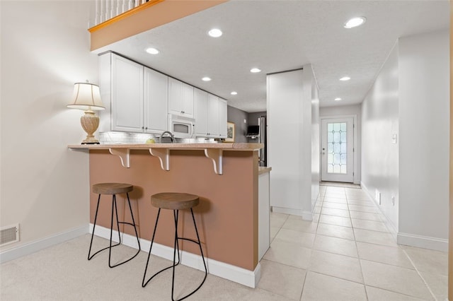 kitchen with kitchen peninsula, a kitchen bar, light tile patterned floors, and white cabinetry