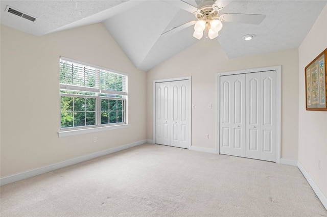 unfurnished bedroom featuring vaulted ceiling, ceiling fan, two closets, and light colored carpet