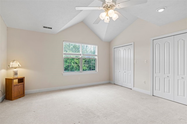 unfurnished bedroom with two closets, light colored carpet, vaulted ceiling, and ceiling fan