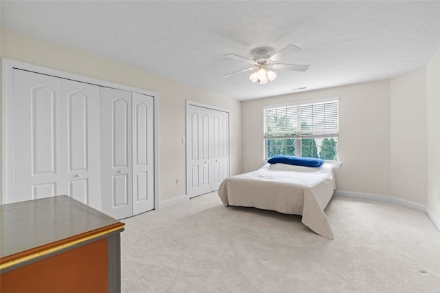 carpeted bedroom featuring multiple closets, a textured ceiling, and ceiling fan