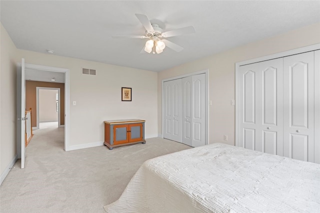 bedroom featuring ceiling fan, multiple closets, and light carpet