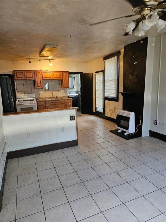 kitchen featuring sink, black fridge, heating unit, light tile patterned floors, and white gas range oven