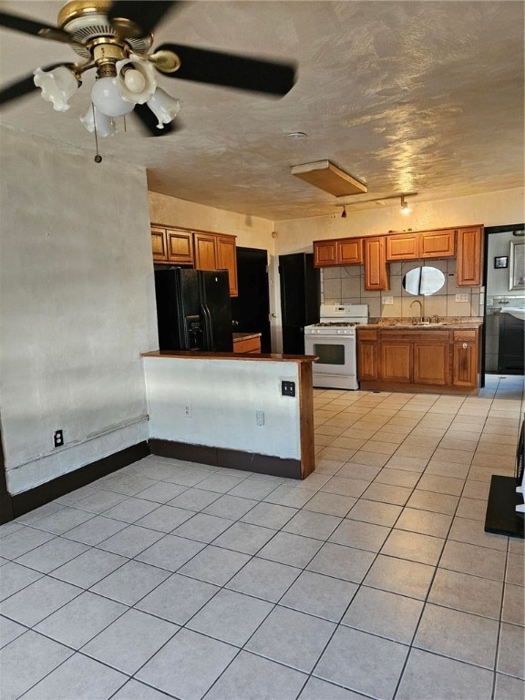 kitchen featuring black fridge, gas range gas stove, ceiling fan, sink, and light tile patterned floors