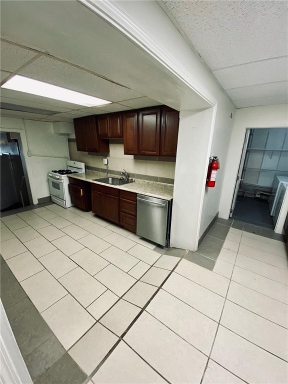 kitchen with sink, light tile patterned floors, stainless steel dishwasher, a drop ceiling, and white range with gas stovetop