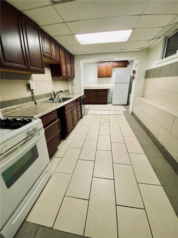 kitchen featuring sink, white appliances, a paneled ceiling, dark brown cabinets, and light tile patterned floors