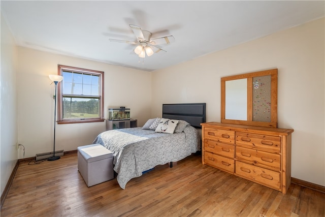 bedroom with hardwood / wood-style flooring, ceiling fan, and a baseboard heating unit