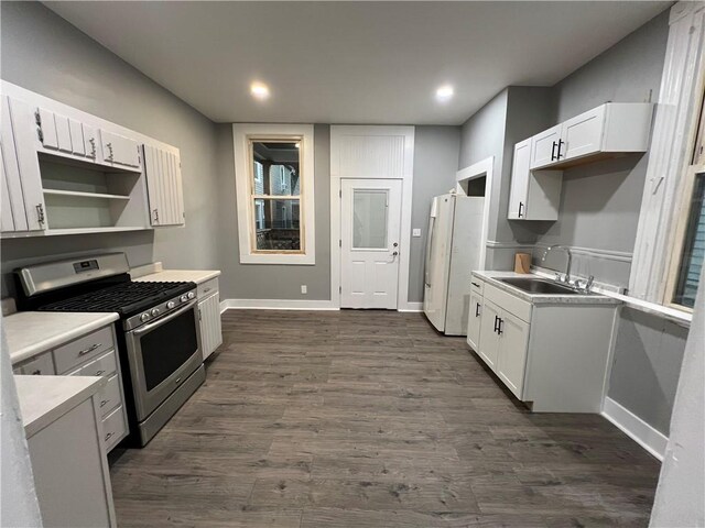 kitchen with white refrigerator, stainless steel gas range oven, dark hardwood / wood-style flooring, sink, and white cabinets