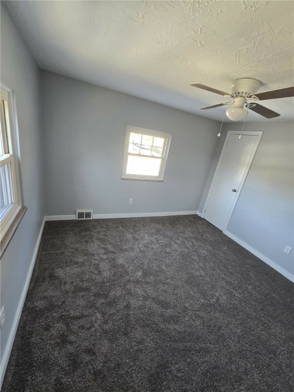 empty room featuring dark colored carpet, ceiling fan, and a textured ceiling