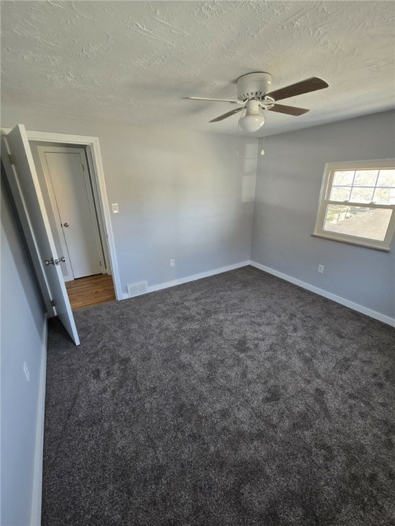 spare room featuring ceiling fan, a textured ceiling, and dark colored carpet