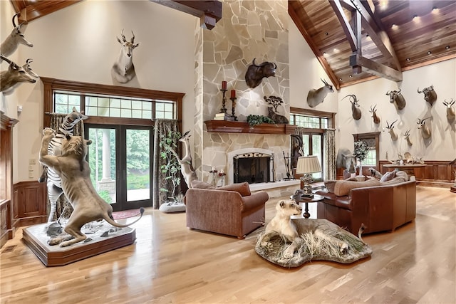 living room featuring light hardwood / wood-style floors, beamed ceiling, wooden ceiling, a stone fireplace, and high vaulted ceiling