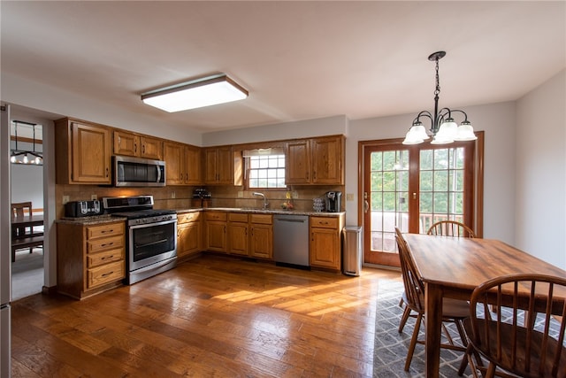 kitchen with appliances with stainless steel finishes, hardwood / wood-style flooring, decorative backsplash, and decorative light fixtures