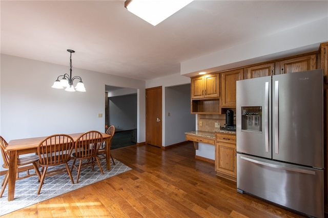 kitchen featuring light stone counters, stainless steel refrigerator with ice dispenser, dark hardwood / wood-style floors, an inviting chandelier, and decorative backsplash