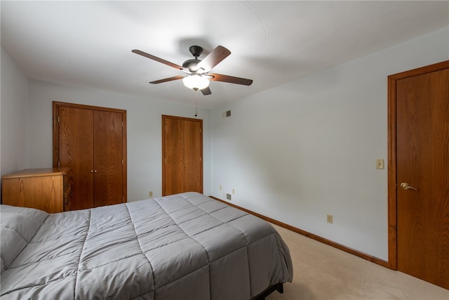 carpeted bedroom with ceiling fan and multiple closets