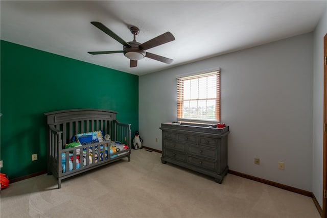 carpeted bedroom with ceiling fan and a nursery area