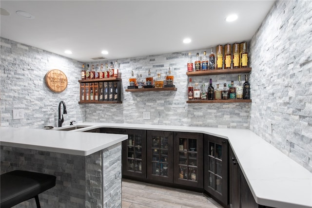 bar with dark brown cabinetry, light hardwood / wood-style flooring, and sink