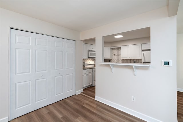 kitchen with appliances with stainless steel finishes, a breakfast bar, dark hardwood / wood-style floors, and white cabinetry