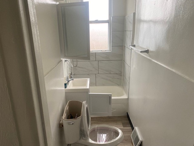 bathroom with wood-type flooring, a washtub, vanity, and toilet