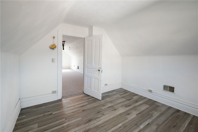 additional living space with a textured ceiling, dark hardwood / wood-style floors, and vaulted ceiling