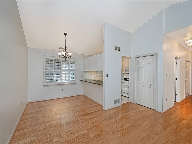 unfurnished living room with light hardwood / wood-style floors, high vaulted ceiling, and an inviting chandelier