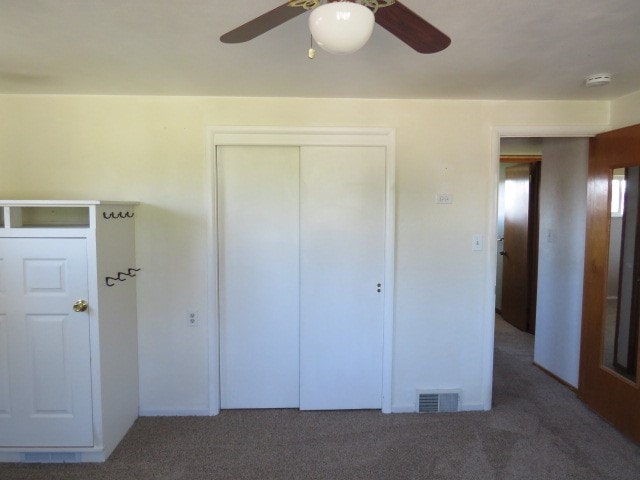 unfurnished bedroom with a closet, dark carpet, and ceiling fan