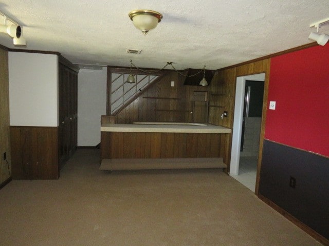 interior space with kitchen peninsula, carpet floors, a textured ceiling, wooden walls, and ornamental molding