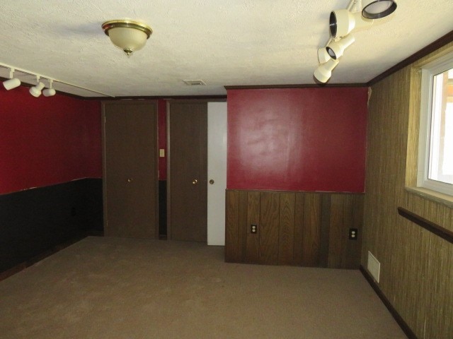 carpeted spare room featuring a textured ceiling, track lighting, and wooden walls