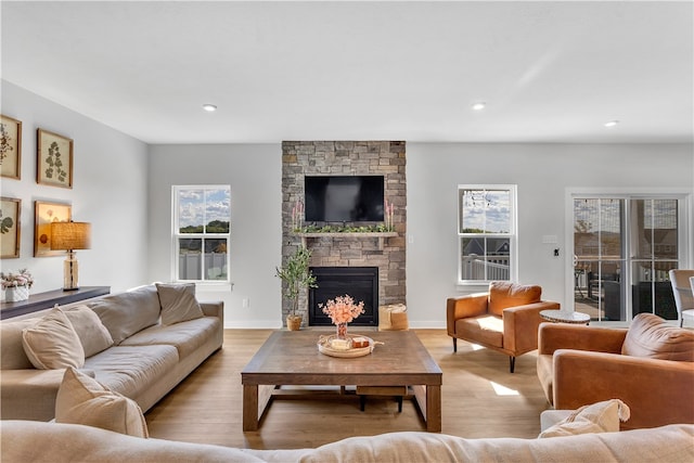 living room featuring a stone fireplace, light wood-type flooring, and plenty of natural light