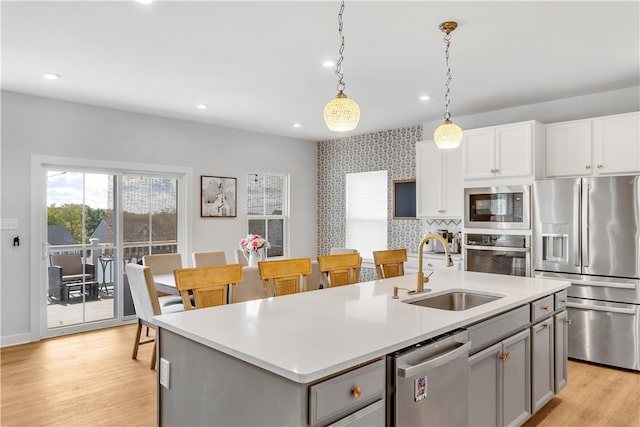 kitchen with light wood-type flooring, a center island with sink, sink, hanging light fixtures, and appliances with stainless steel finishes