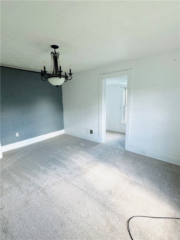 carpeted empty room featuring an inviting chandelier and a textured ceiling