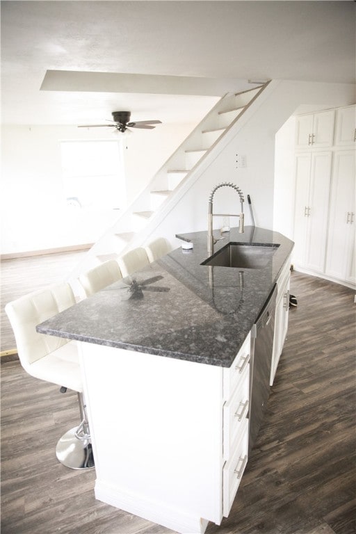 kitchen with an island with sink, dark stone countertops, sink, and white cabinetry