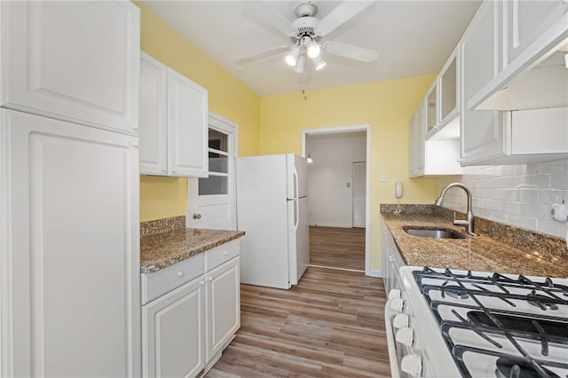 kitchen with light wood-type flooring, sink, white appliances, white cabinetry, and dark stone counters