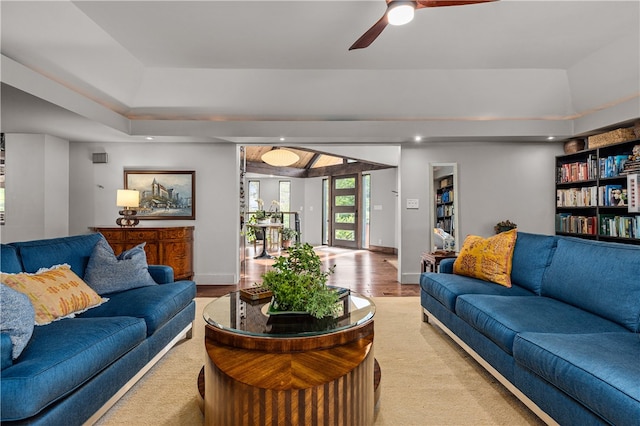 living room featuring ceiling fan, a tray ceiling, and light hardwood / wood-style flooring