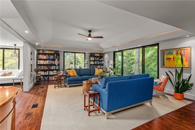 living room featuring wood-type flooring, a tray ceiling, and plenty of natural light