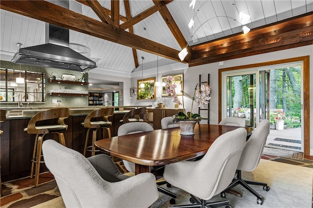 carpeted dining area with bar area, beam ceiling, and high vaulted ceiling