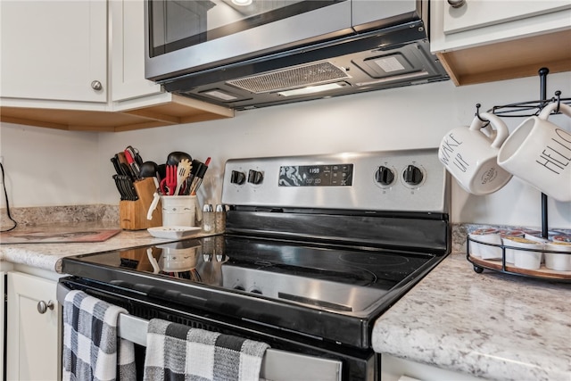 kitchen with appliances with stainless steel finishes, light stone counters, and white cabinetry