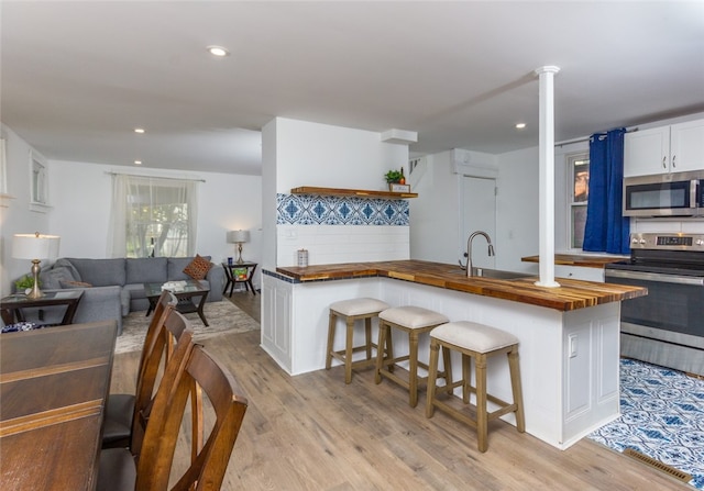 kitchen with butcher block countertops, appliances with stainless steel finishes, light wood-type flooring, and a kitchen breakfast bar