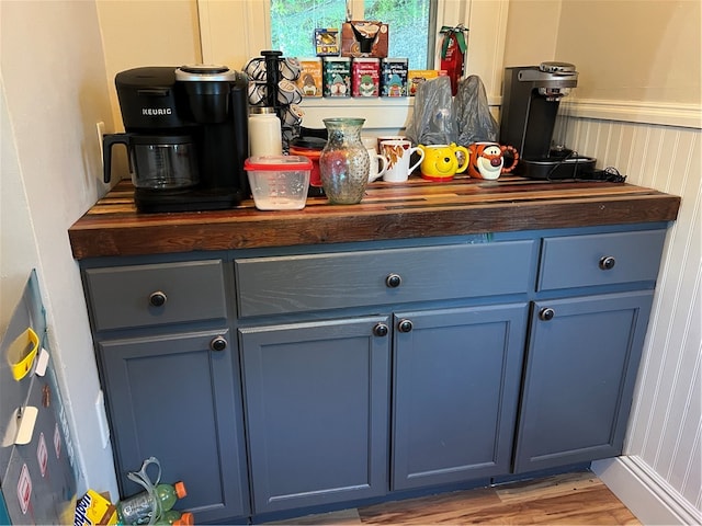 bar with blue cabinets, light hardwood / wood-style flooring, and wood counters