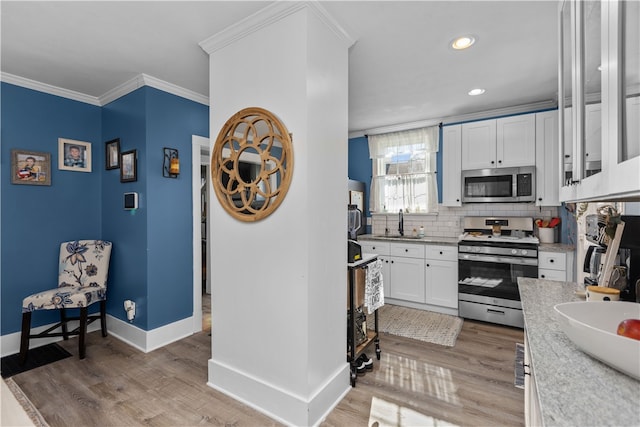 kitchen with stainless steel appliances, wood-type flooring, ornamental molding, and white cabinets