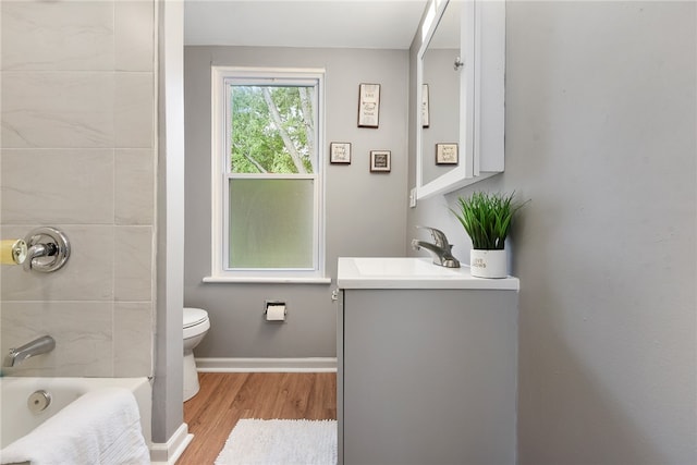 full bathroom with wood-type flooring, tiled shower / bath, vanity, and toilet