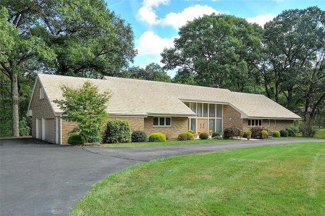 view of front of home featuring driveway, a front lawn, stone siding, and an attached garage