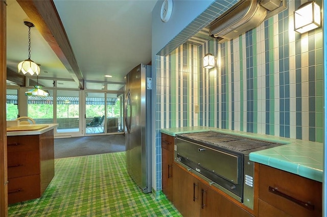 kitchen with freestanding refrigerator, carpet floors, brown cabinets, pendant lighting, and beamed ceiling