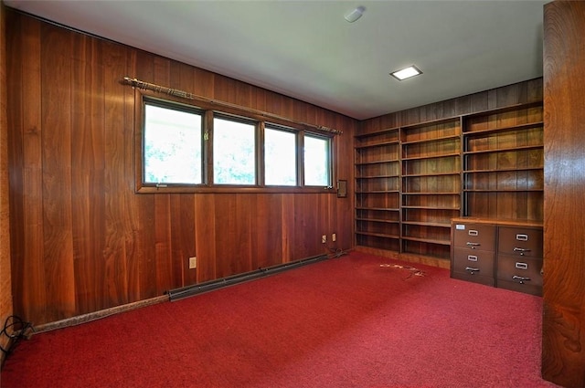 unfurnished office featuring wooden walls, carpet floors, baseboard heating, and built in shelves