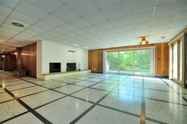unfurnished living room with inlaid floor details, wood walls, a brick fireplace, and a drop ceiling