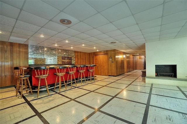 indoor dry bar with inlaid floor details, recessed lighting, a large fireplace, wood walls, and a paneled ceiling