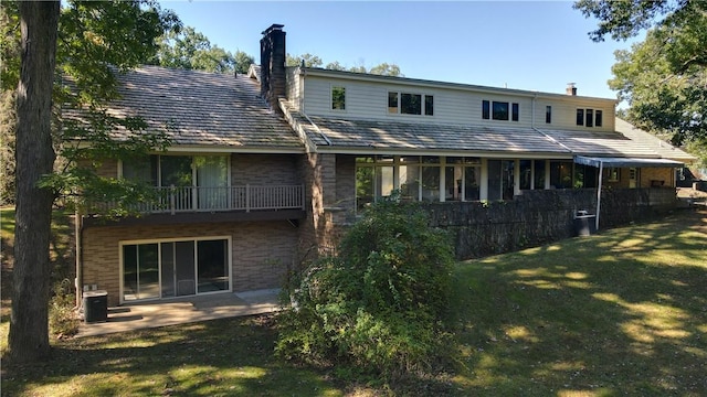 rear view of property with a chimney, a lawn, a balcony, brick siding, and central air condition unit