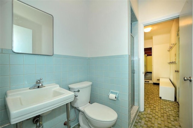 bathroom featuring a sink, a stall shower, toilet, tile walls, and a wainscoted wall