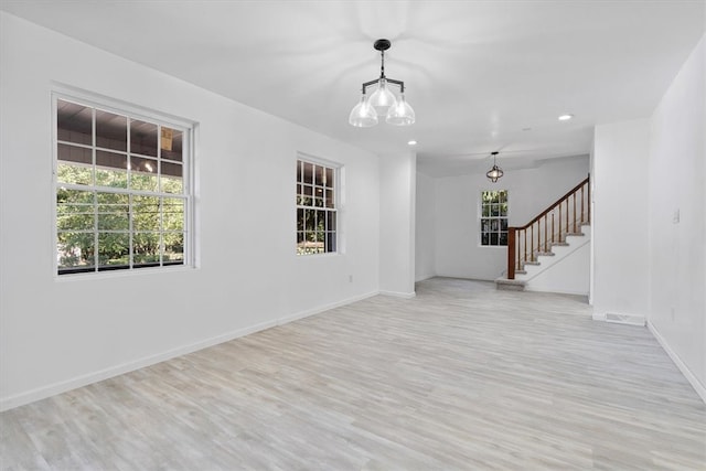 spare room featuring a notable chandelier and light wood-type flooring